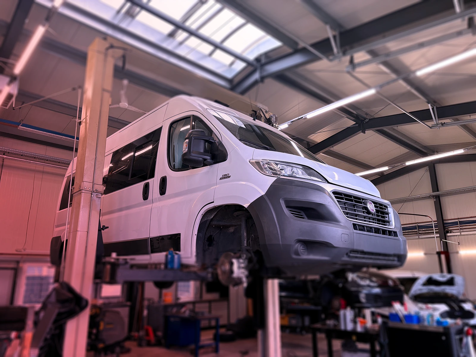 Reisemobil-Service - Weißes Reisemobil (Wohnwagen) auf der Hebebühne hochgefahren.